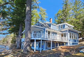 Three story blue home with white trim overlooking the lake.
