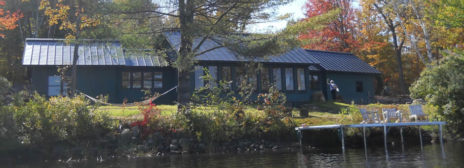 Waterfront home with metal roofing, large windows overlooking the lake and dock. 